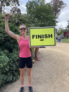 A woman in running gear holds up a "Finish" sign with her arm in the air, celebrating completing a run